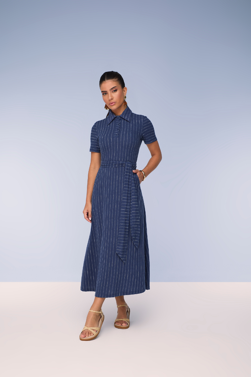 Mulher vestindo um elegante vestido listrado midi com acessórios sofisticados em um ambiente luxuoso.