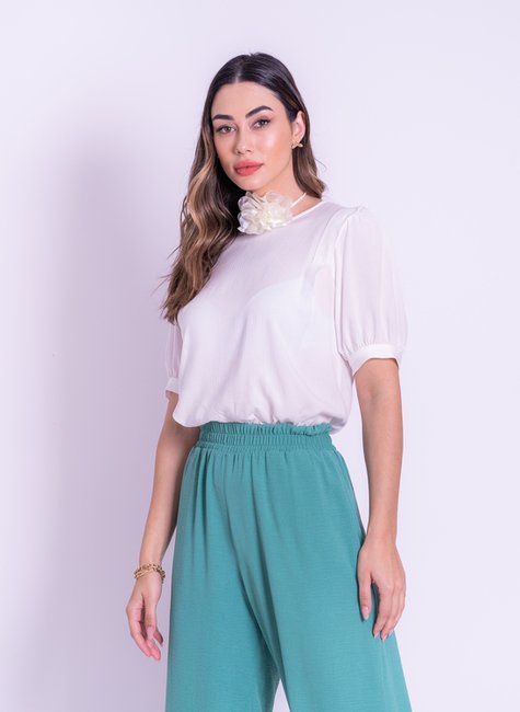 modelo usando uma blusa branca lisa com mangas mais alongadas (antes do cotovelo) e fechamento de botão no punho da blusa