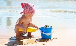 bebê na praia brincando com balde e areia