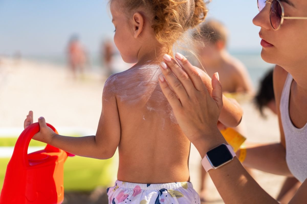 mae passando protetor solar em bebe na praia