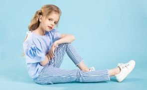 garotinha sentada usando roupas da moda infantil em fundo azul