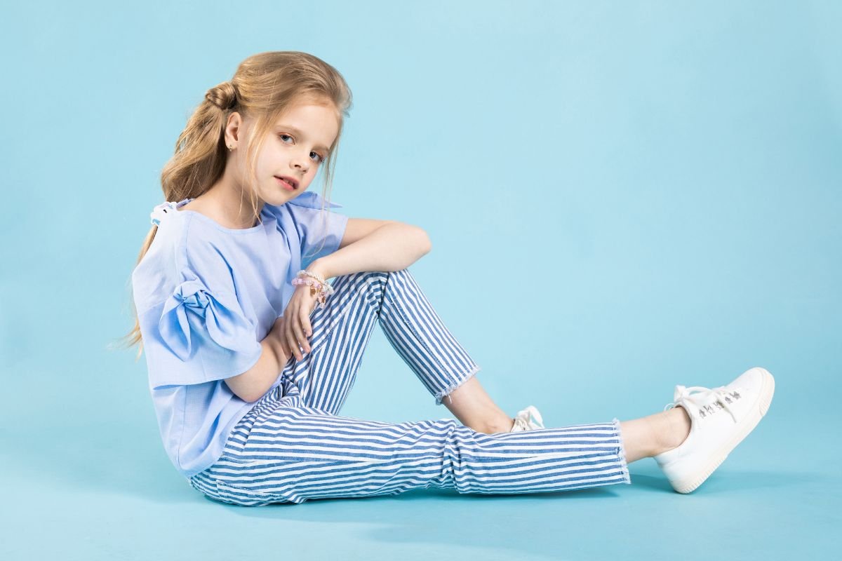 garotinha sentada usando roupas da moda infantil em fundo azul