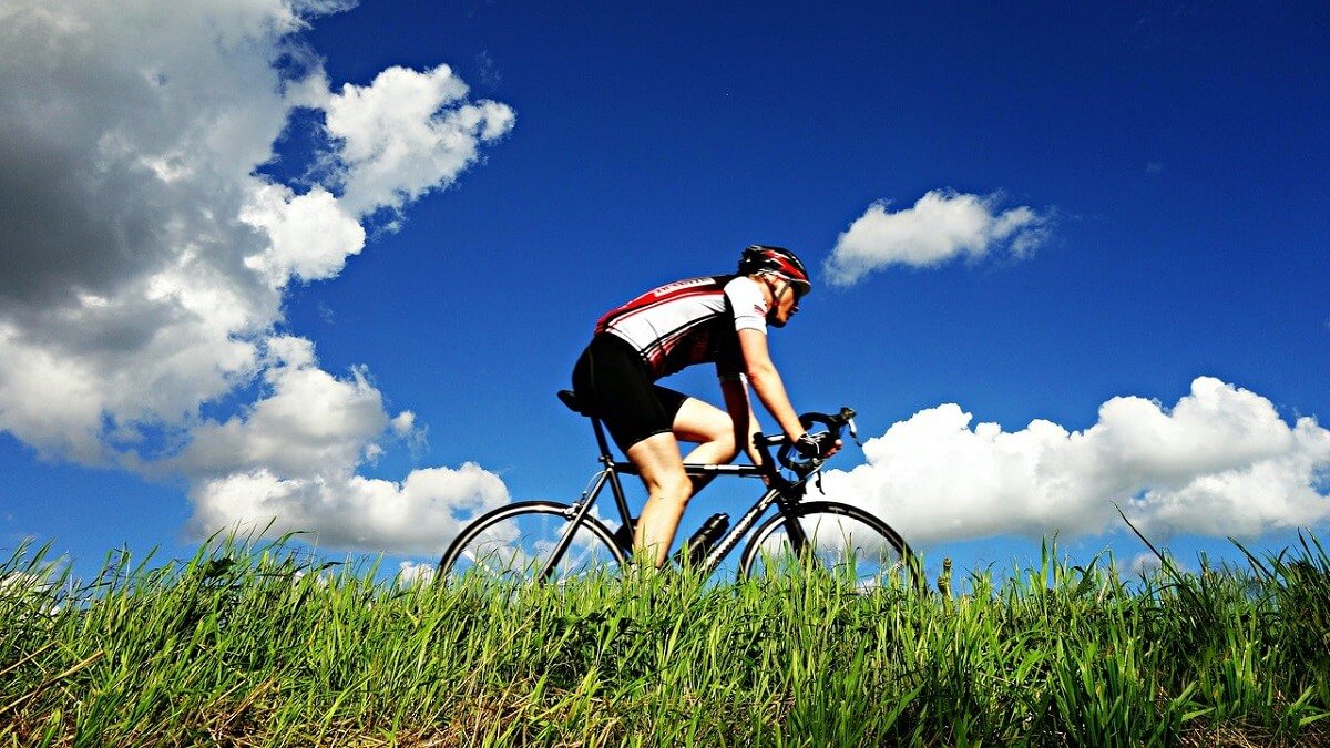 Homem pedalando com céu azul e nuvens ao fundo