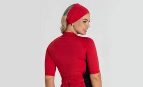 Mulher com bandana como faixa na cabeça, da mesma cor que seu traje de ciclismo vermelho