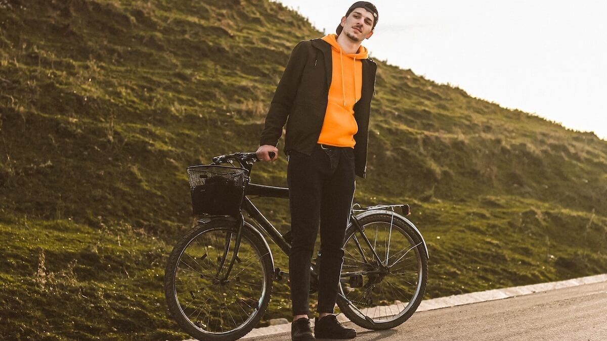 Homem com roupa preta e moletom laranja, ao lado da bicicleta